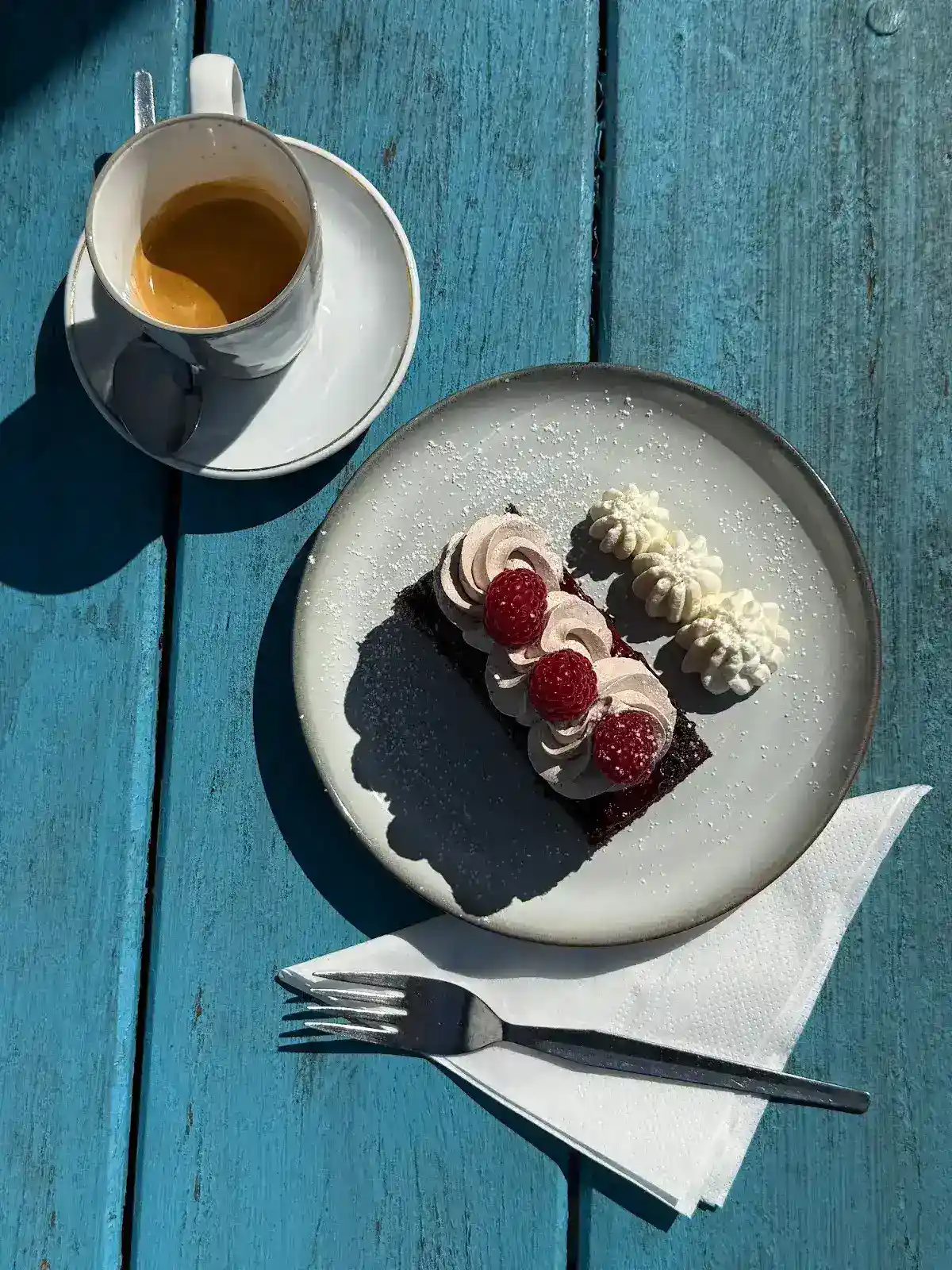 Chocolate brownie with raspberries and cream on a blue outdoor table with espresso